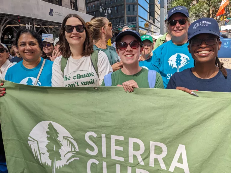 A diverse group of Sierra Club staff and volunteers hold a large green banner with Sierra Club's logo at the March to End Fossil Fuels.
