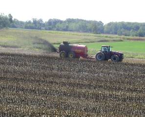 A tractor hauls a tank spewing black liquid manure over a field.