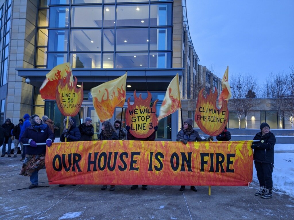 photo of protesters holding a banner that says, "Our House is on Fire"