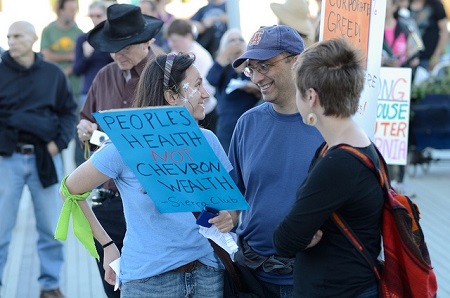 Smiling people holding protest signs "Peoples Health Not Chevron Wealth - Sierra Club"