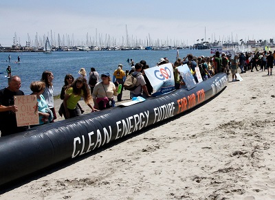 People holding signs and standing in a line on a beach near the water