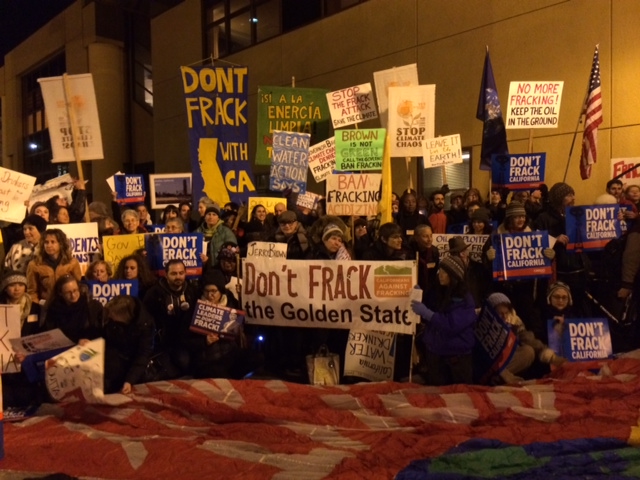 Fracking protestors holding signs in a street at night