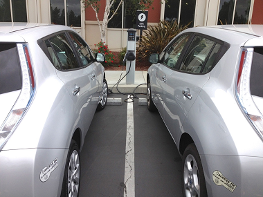 View from behind two grey electric vehicles charging up at an office complex