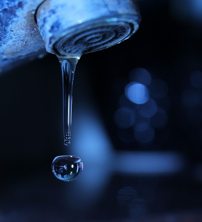 Old indoor water faucet with long water droplet, all in deep blue tones