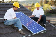Two workers on a rooftop holding a solar panel