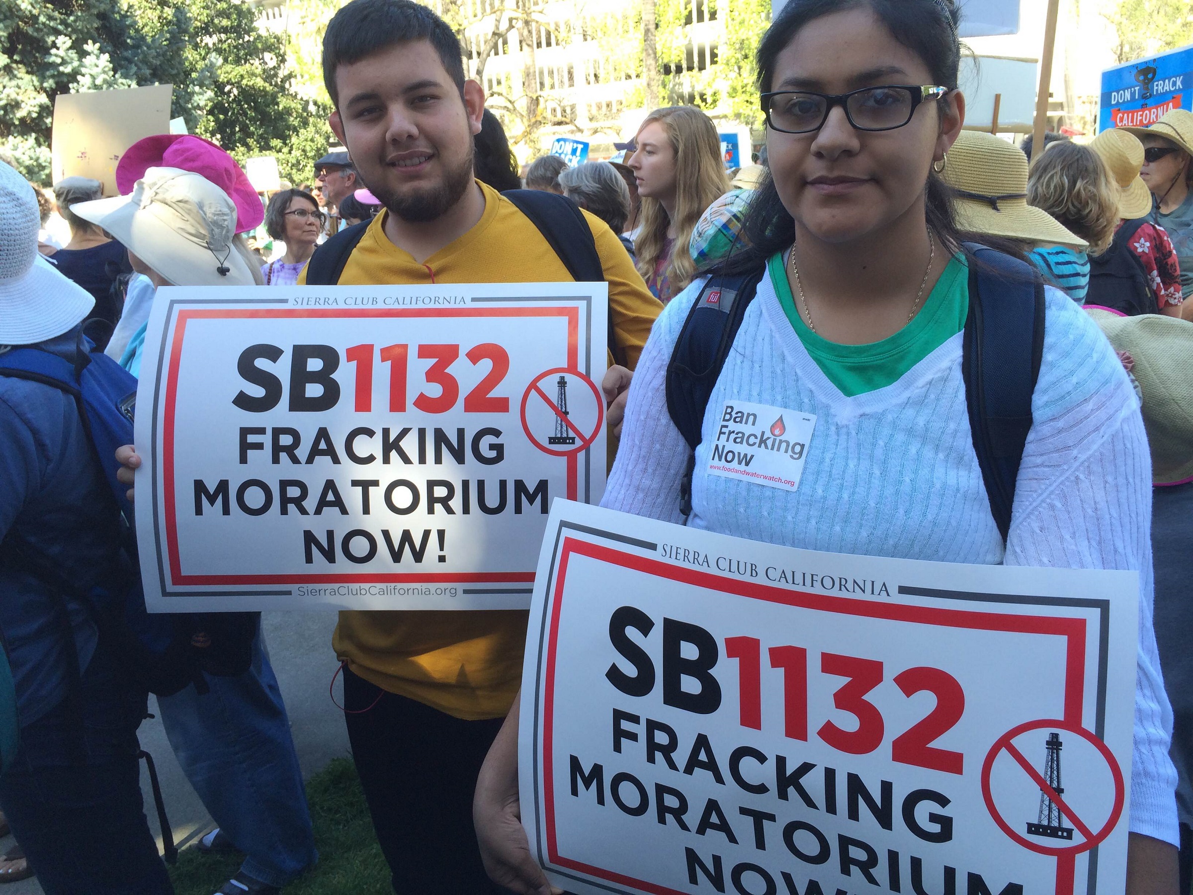 Young man and woman with determined faces holding signs for SB 1132, against fracking