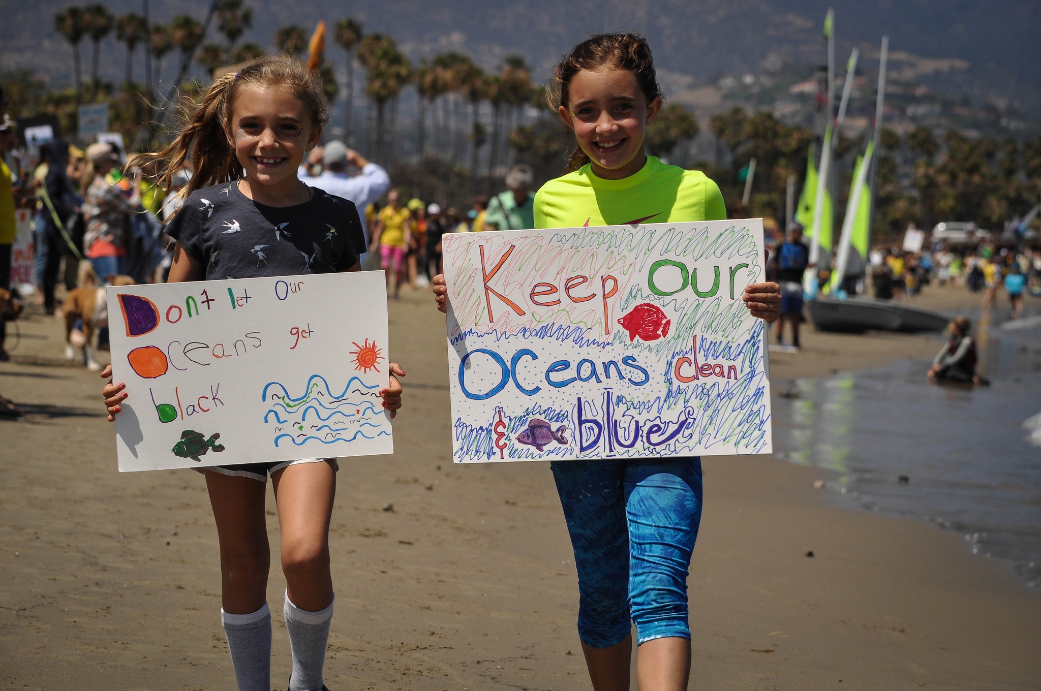 Two elementary-aged girls walking on the beach carrying Keep Our Oceans Blue signs
