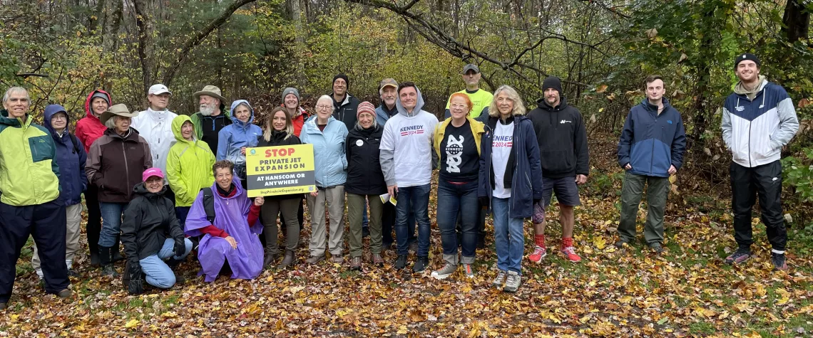 A group of people standing with a campaign sign and a forest behind them