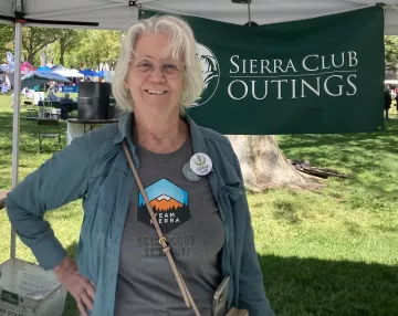 Barbara Leary smiling at the camera while in front of a Sierra Club Outings banner in a park. 