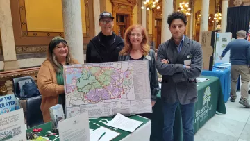 Four people stand at a table at the Indiana Statehouse. They are standing around a map.