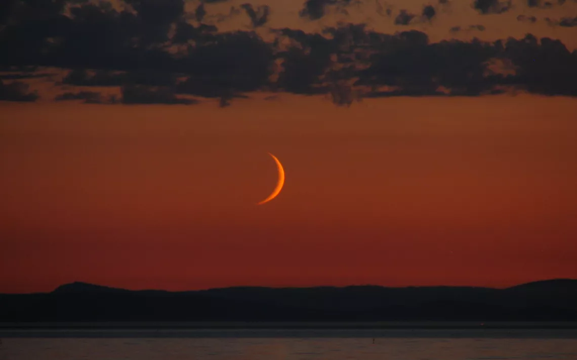 A crescent moon in the warm sunset glow.