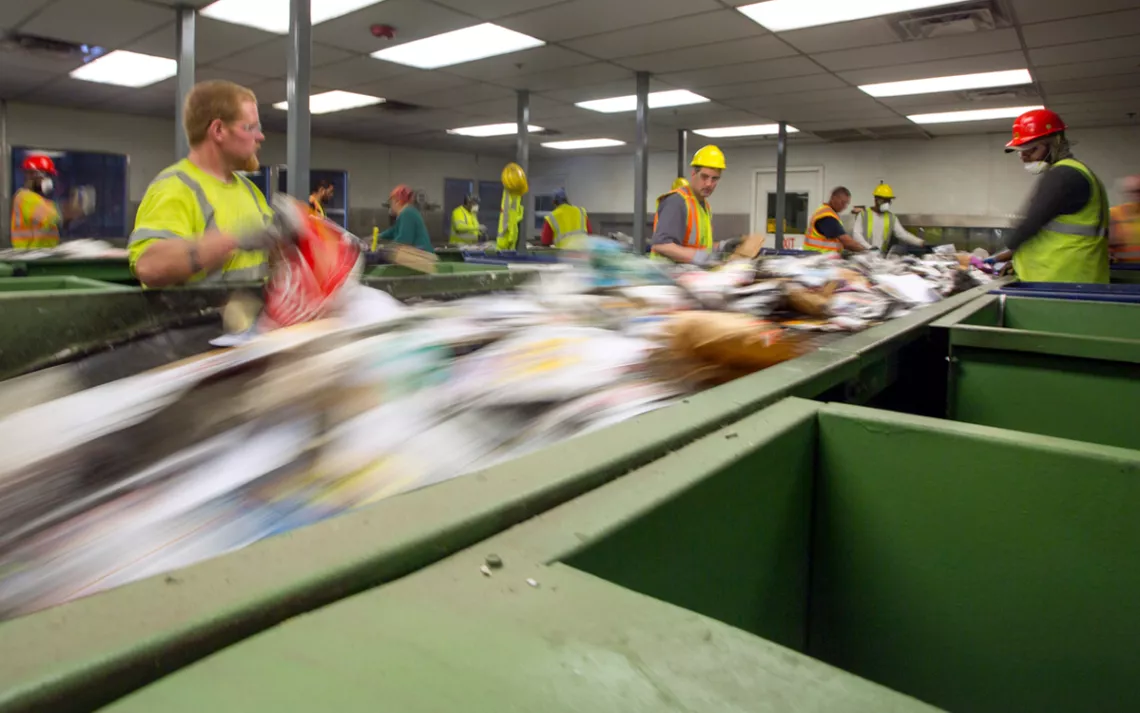 Workers in Portland Maine sort paper at Ecomaine recycling plant to remove contaminated recycling from the waste stream.