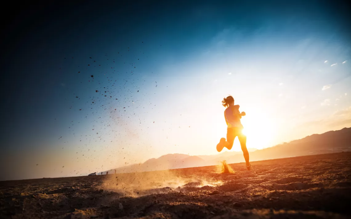 A runner silhouetted against a desert landscape as the sun sets or rises. 