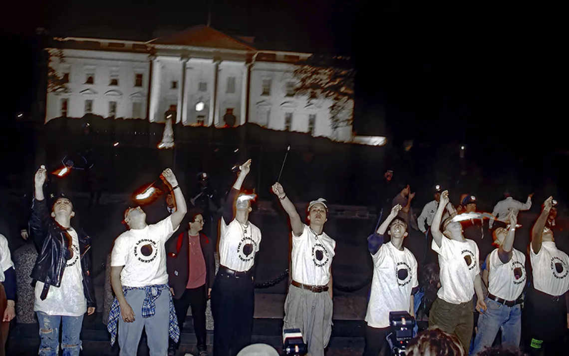 Women in white t-shirts eating fire in front of the White House in the night.