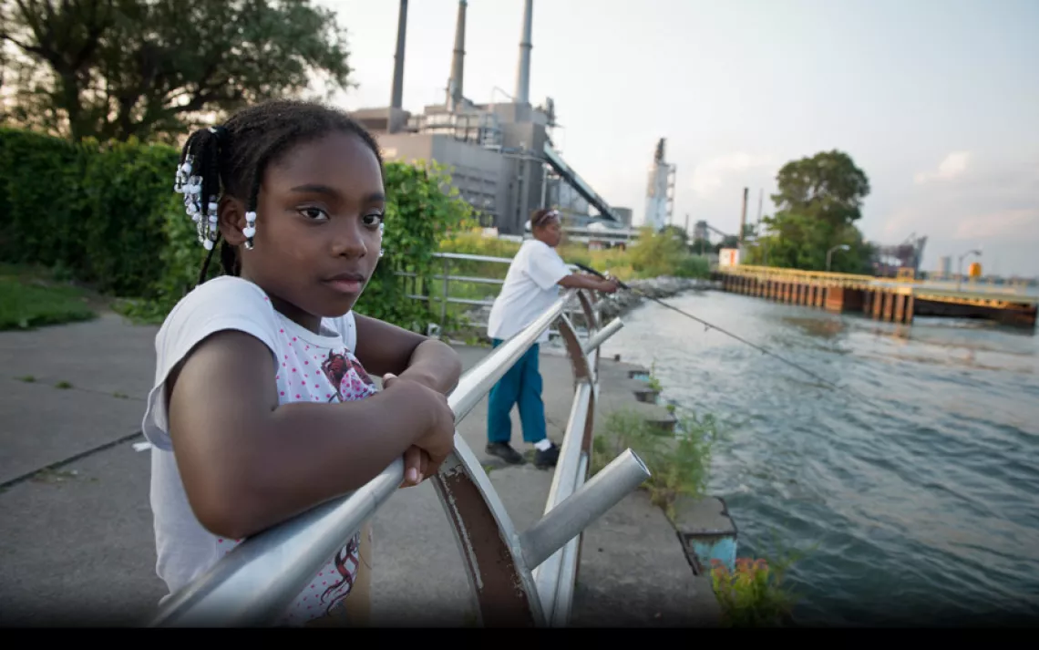 At Belanger Park, Jada Lyons watches friends fish in the Detroit River. The coal-fired River Rouge Power Plant looms in the background. | Ami Vitale/Panos Pictures