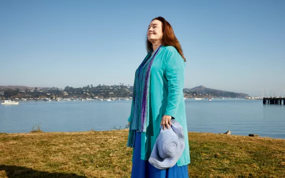Mary Crowley, wearing bright blue and turquoise, stands by the bay in Sausalito.