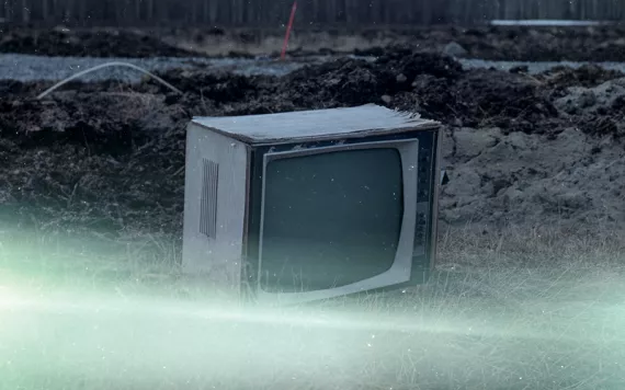 An old TV sits on the ground with a forest in the background.