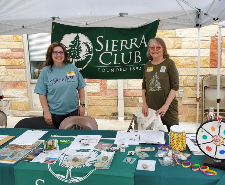 Two women are standing by a table outdoors with a banner reading Sierra Club Hoosier Chapter