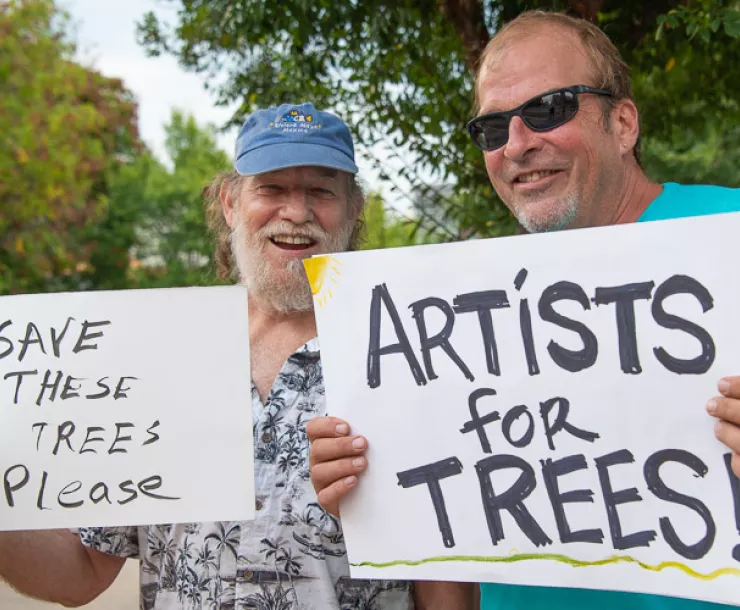 Two smiling men hold signs in support of trees