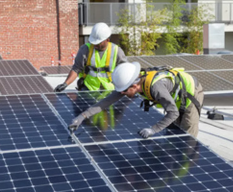 Workers maneuver solar panels as they work install the panels on a roof.