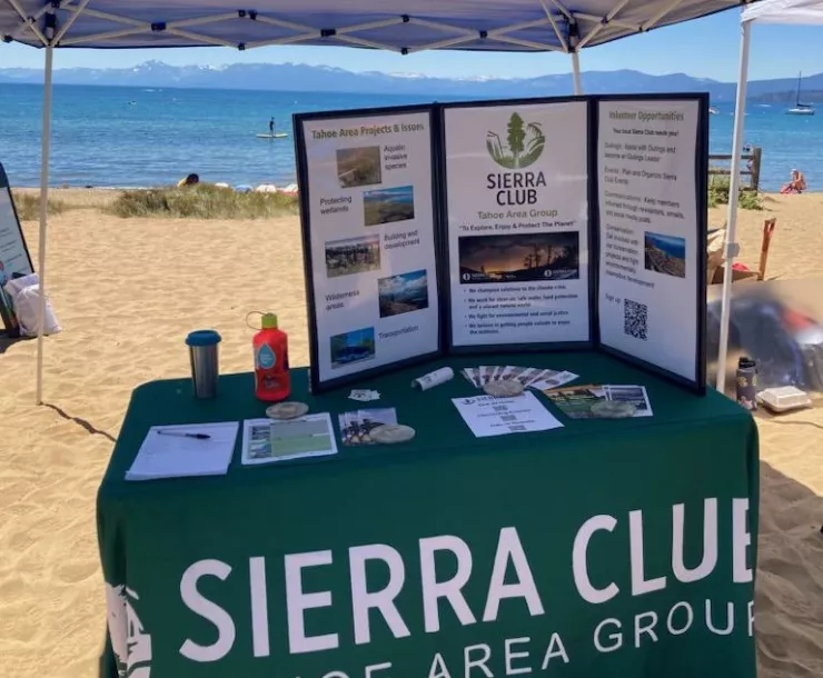 Sierra Club Tahoe Area Group table at 27th Annual Lake Tahoe Summit with sand and Lake Tahoe in the background