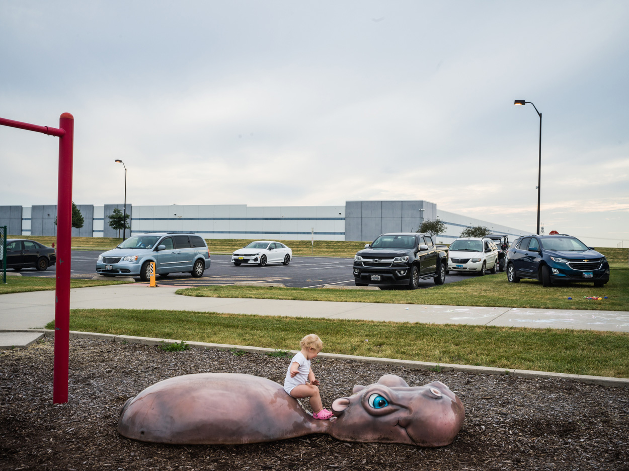 A toddler at a playground located next to a warehouse distribution center.