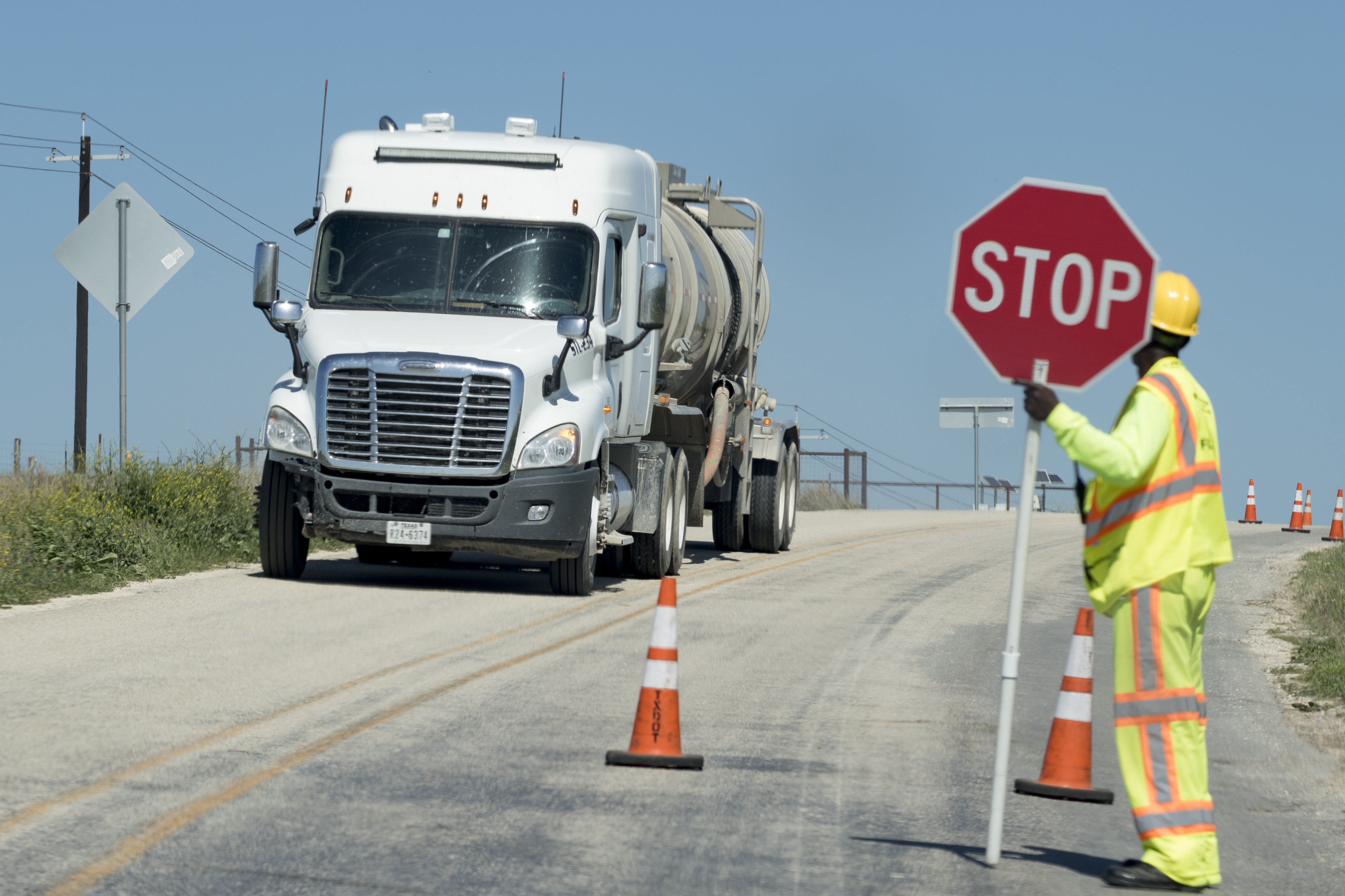 White cement rucks drives down road. A worker with a safety holds a stop sign 