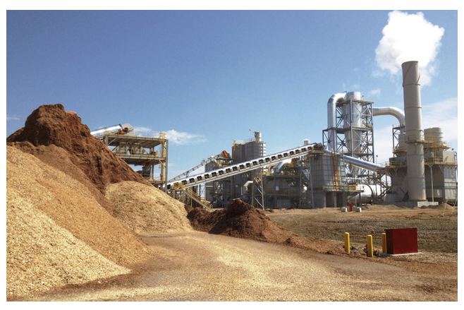 Wood pellet plant with piles of pellets and factory in the background.