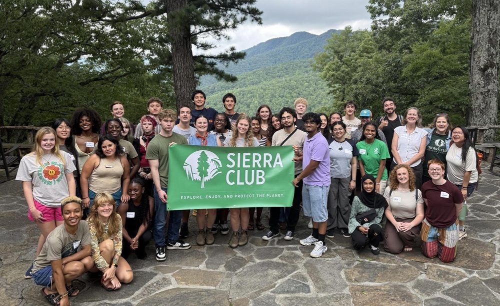 A group of people pose for a photo in western North Carolina, holding a Sierra Club banner with a mountain landscape behind them