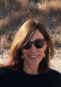 Vaughn Millner head shot with grassy background (white woman with long hair and sunglasses smiling at the camera)