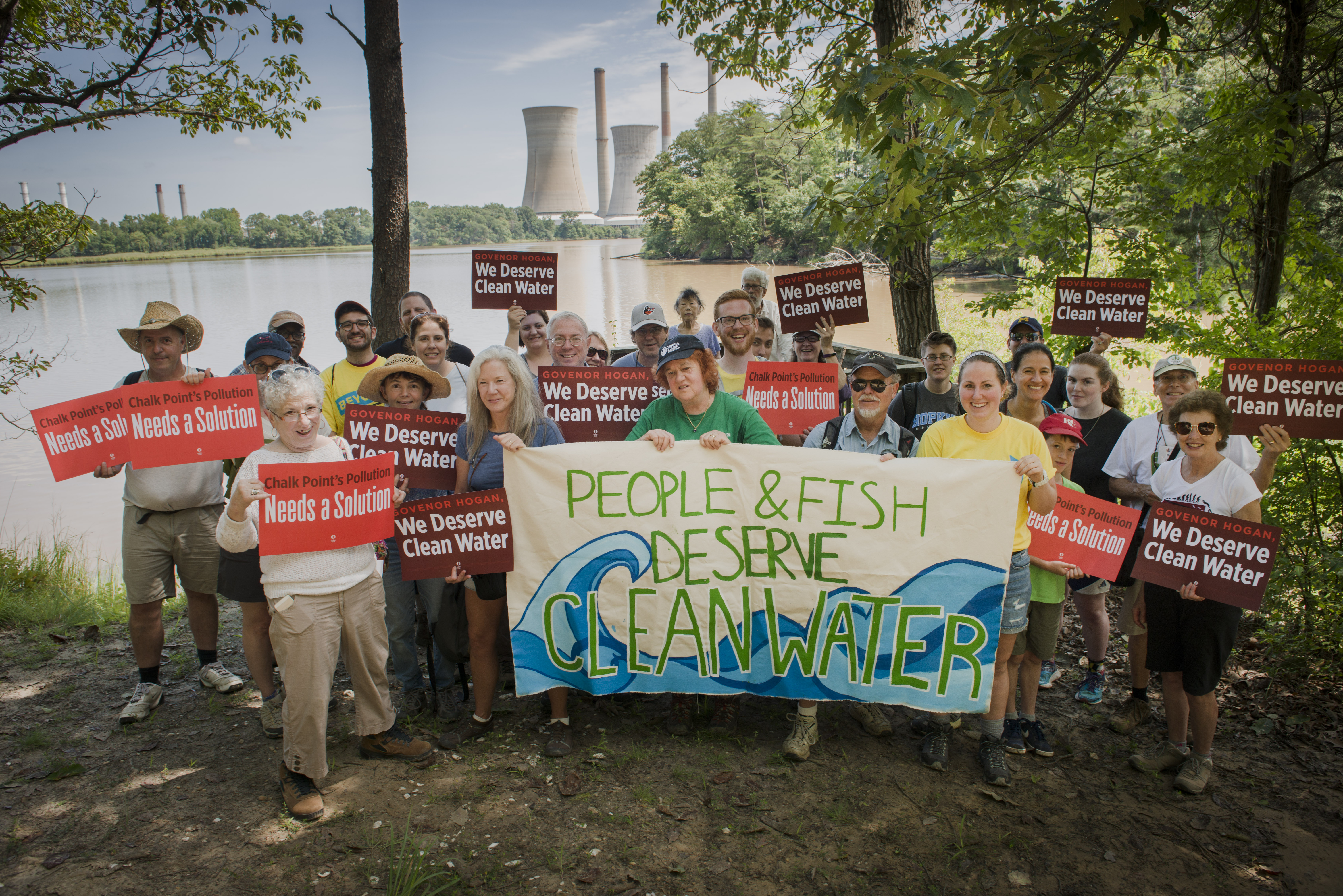 Marylanders gather for a photo in front of the Chalk Point Coal Plant holding a banner that says "People & Fish Deserve Clean Water!"