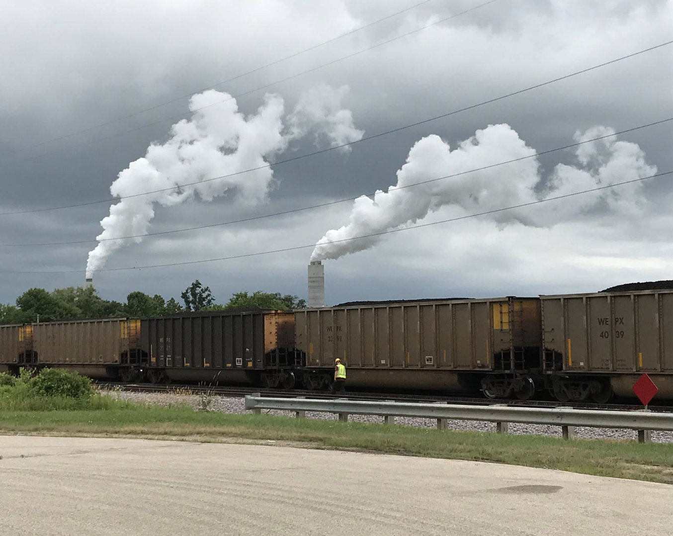 A train delivering coal passes in front of plumes of smoke coming from the Oak Creek plant