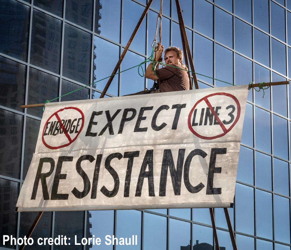 A protester waves a sign that reads "expect resistance" -- with Enbridge and Line 3 crossed out