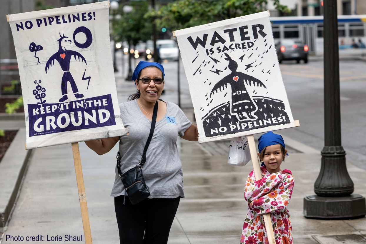 Protesters hold up signs reading "No pipelines" and "Water is sacred"