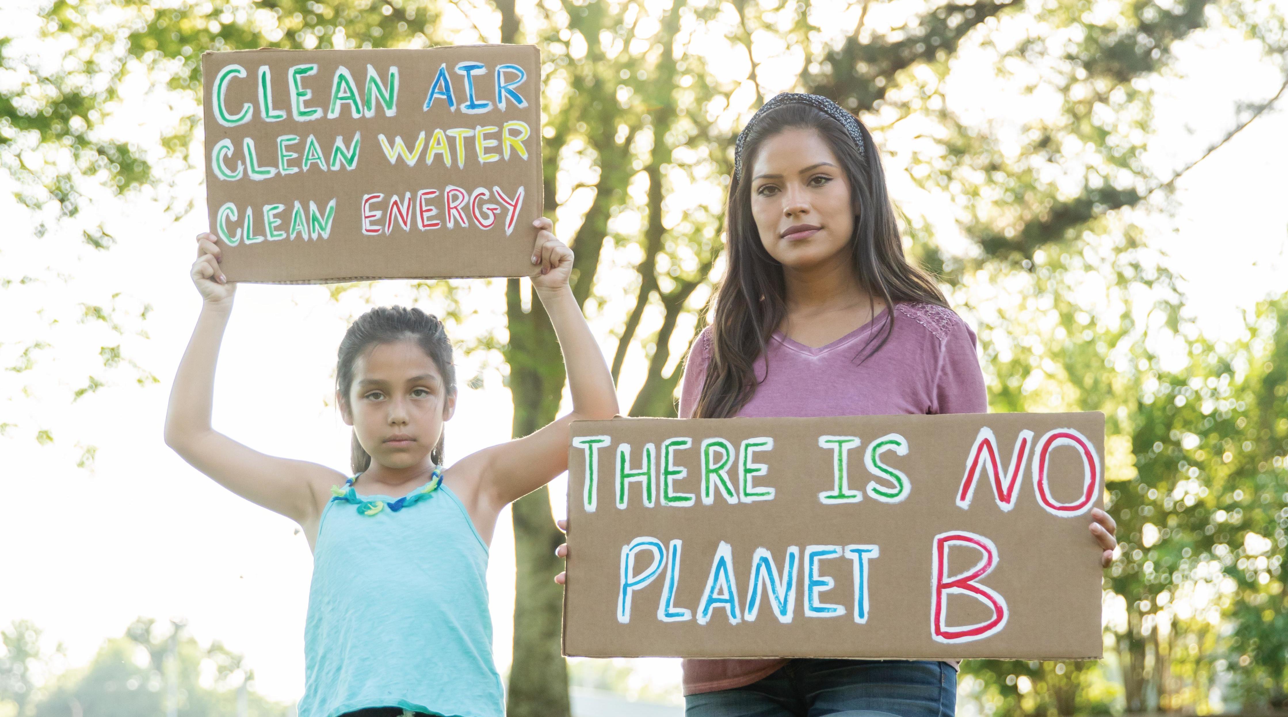 Two youth activists holding signs saying "clean air, clean water, clean energy" and "there is no planet B"
