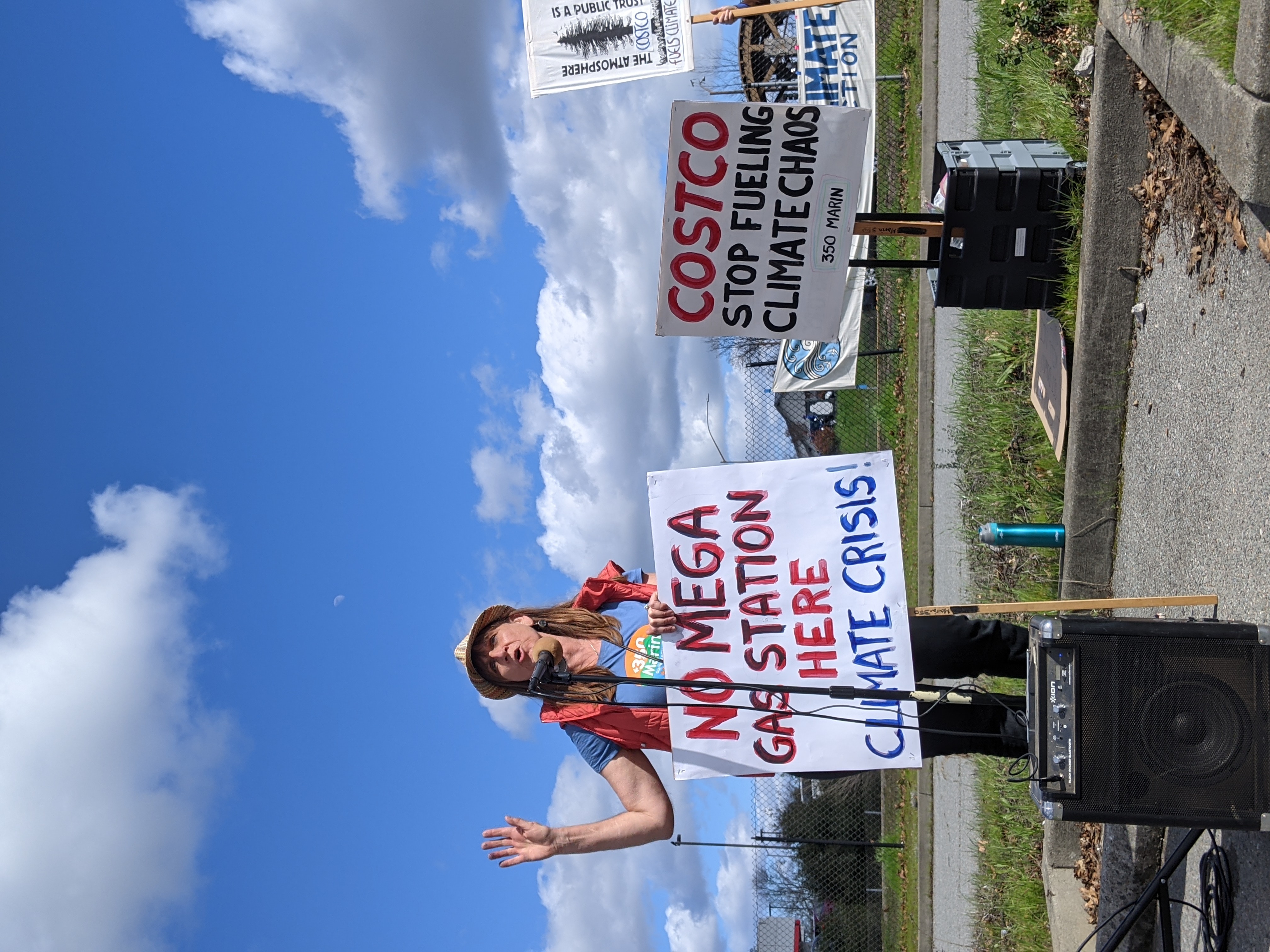 Activists speaking and holding signs at rally against Novato gas station.