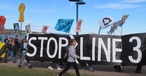 Protest march with banner reading "Stop Line 3"