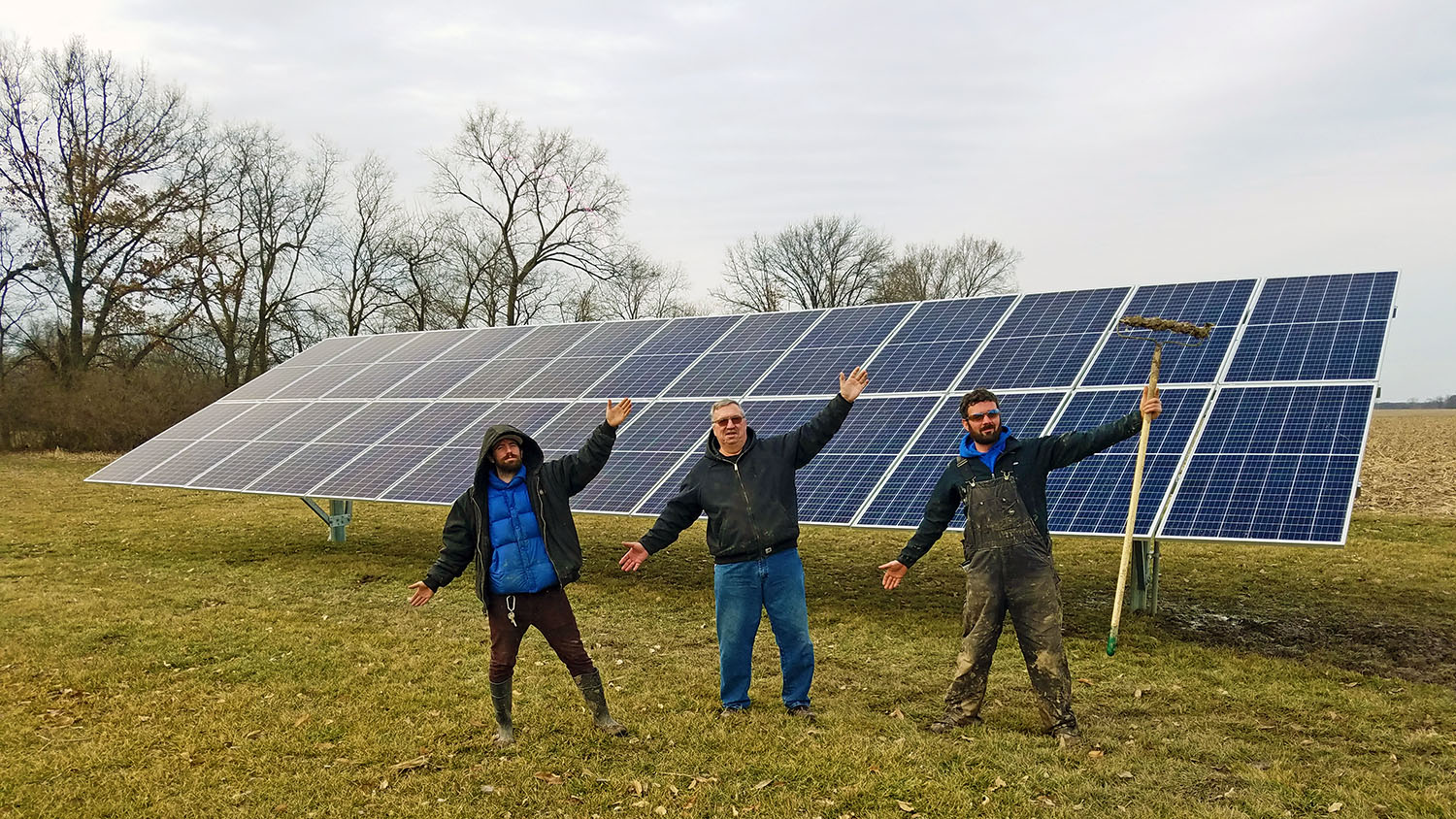 Three people stand in front of a large solar panel.