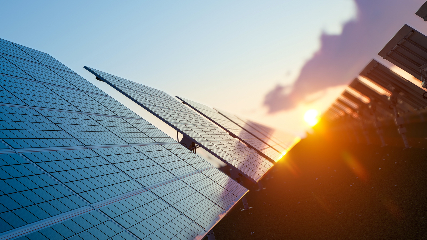 An image of a row of solar panels with the sun rising on the horizon