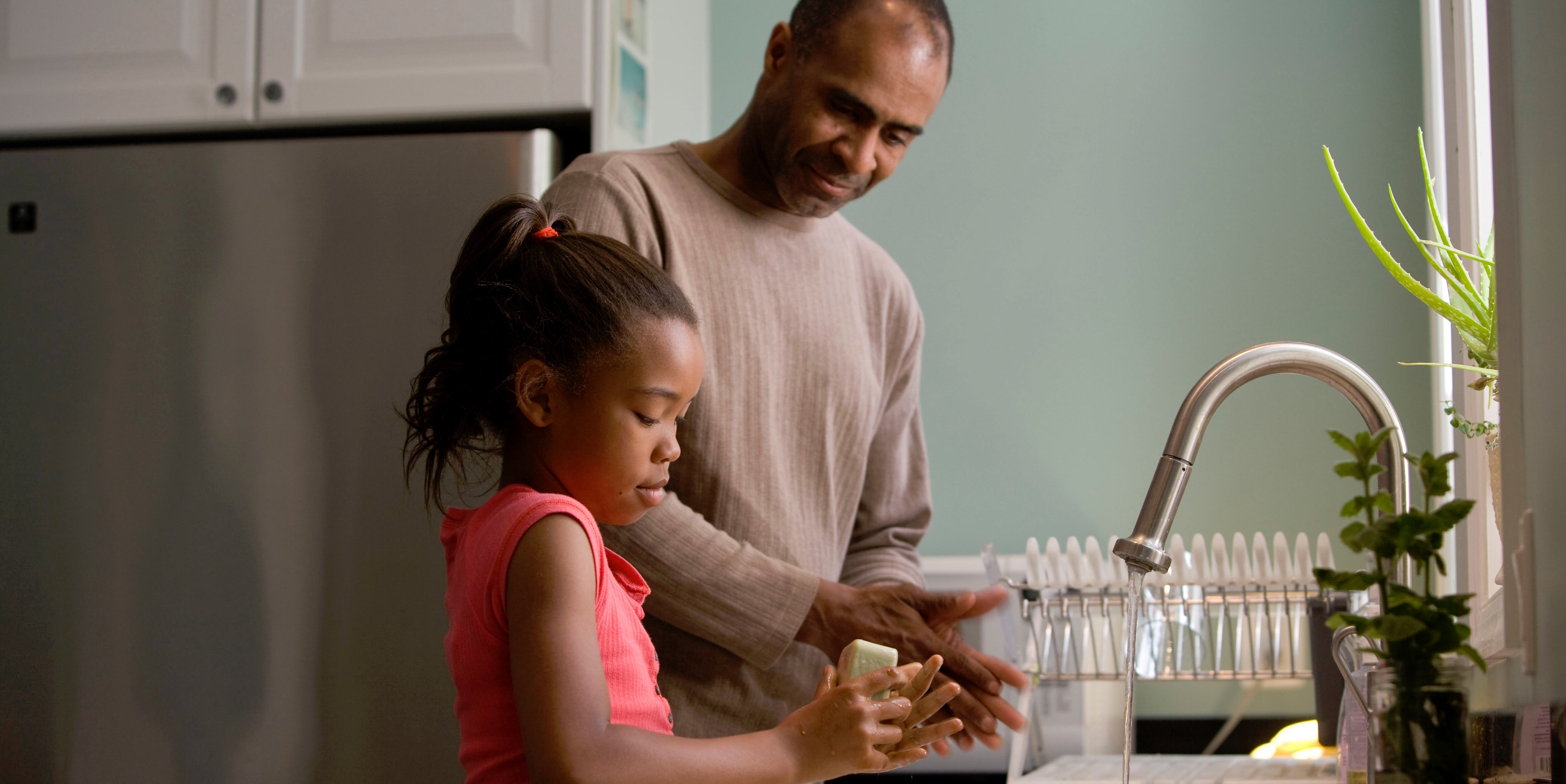 A man and his daughter practice washing their hands at the sink.
