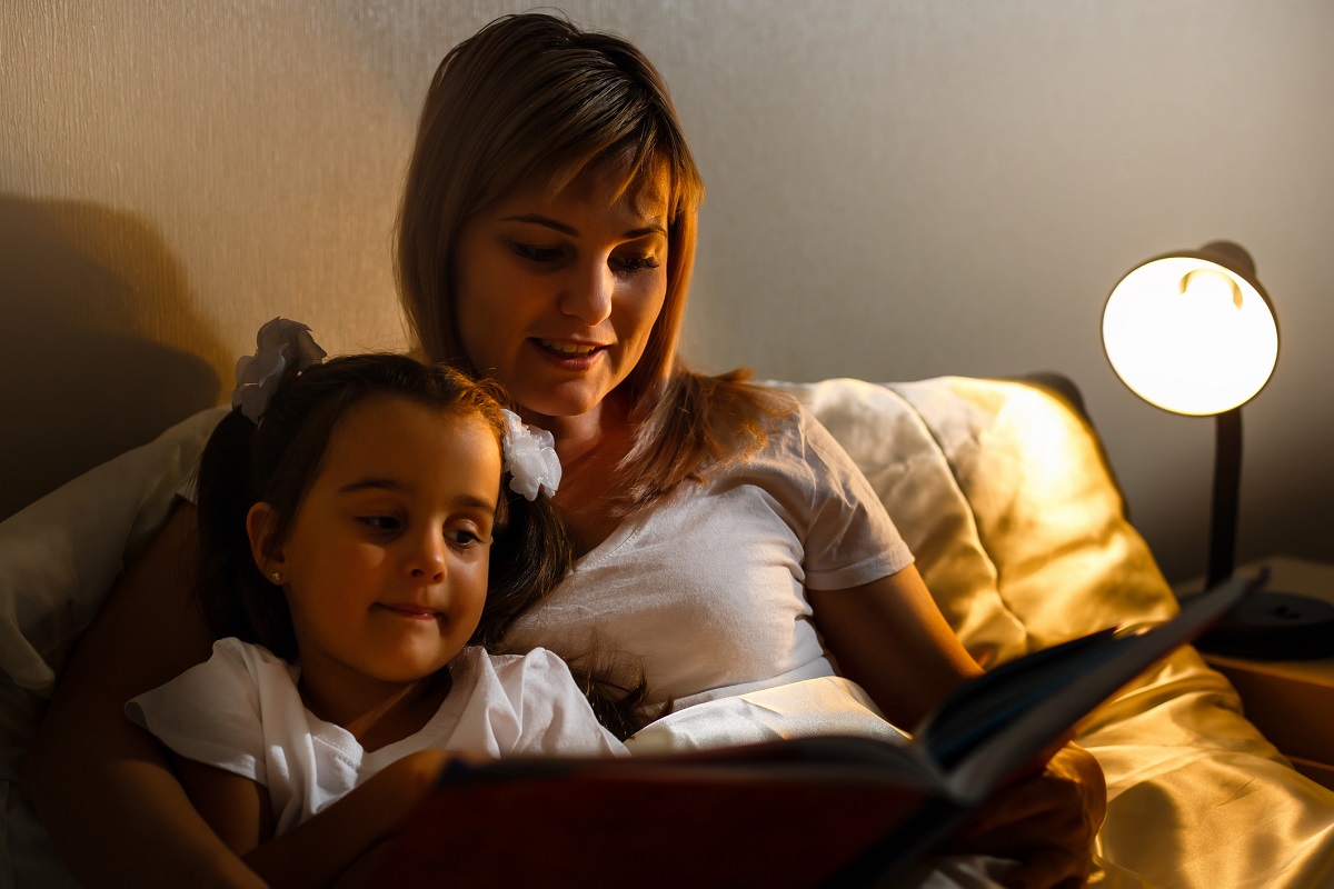 A mother and daughter reading a book together by lamplight