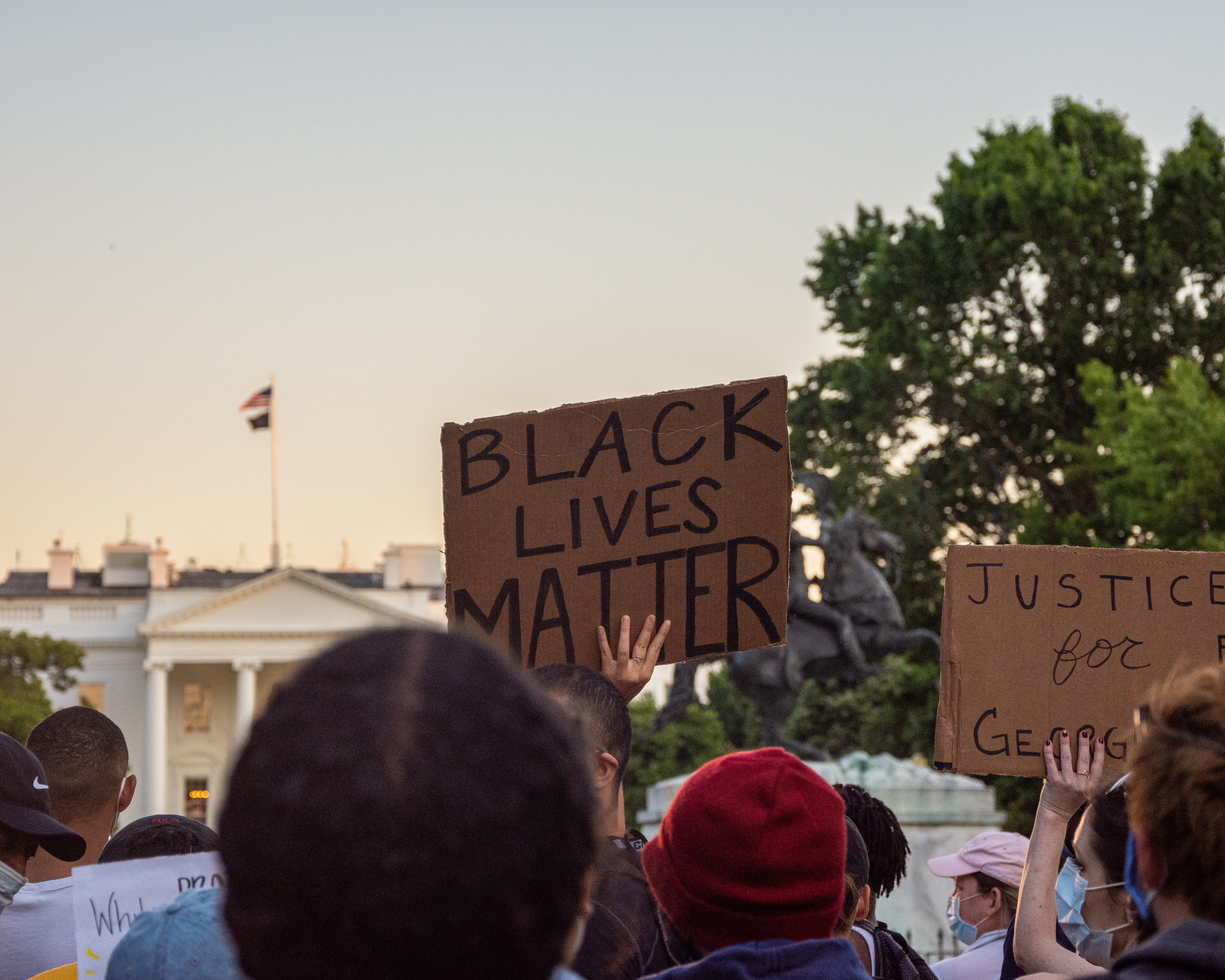 A protest in front of the White House. A sign says "Black Lives Matter." Another says "Justice for George Floyd." 
