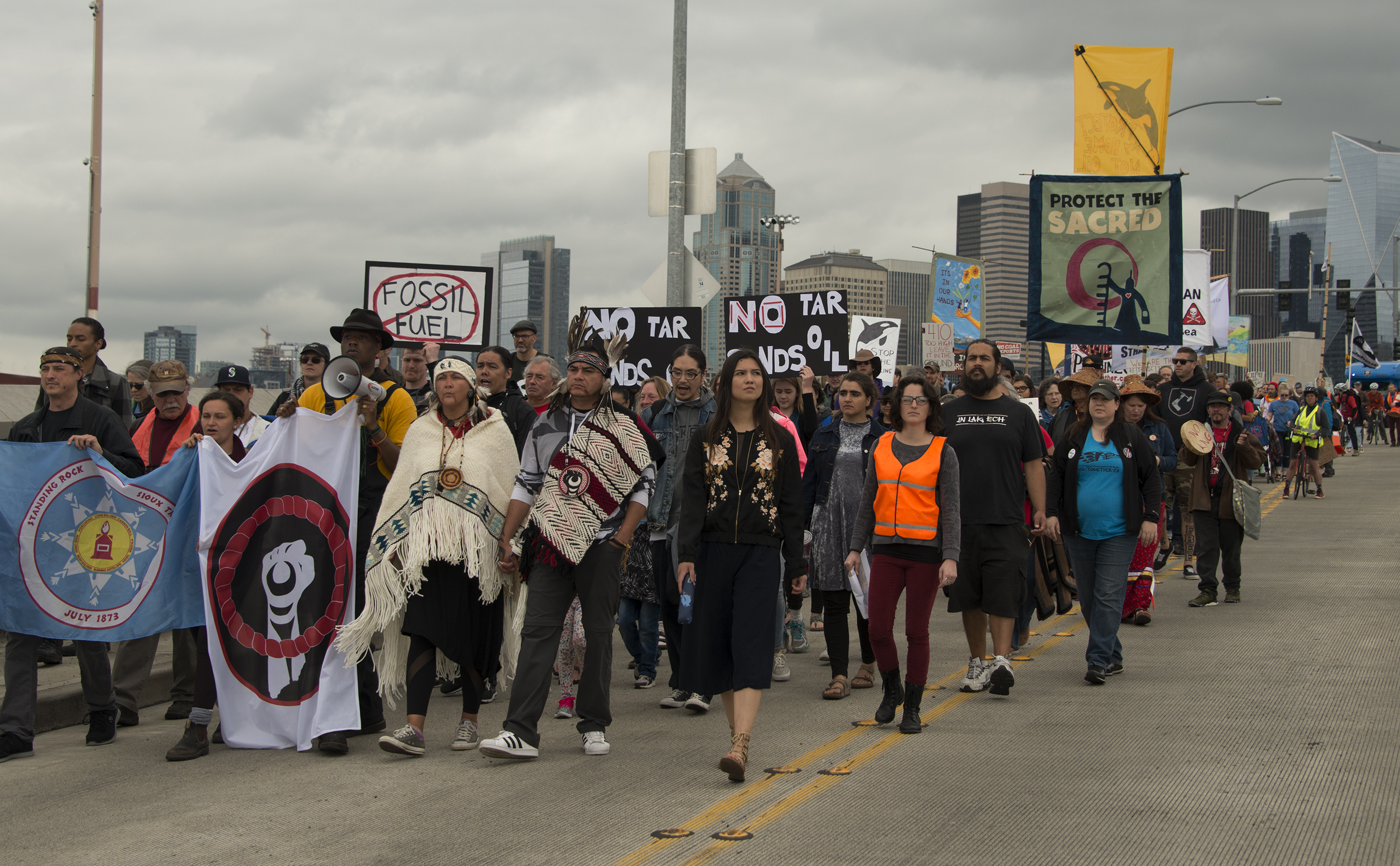 A group of indigenous protestors crossing a bridge holding colorful signs in protest of Fracked Gas and Fossil Fuels