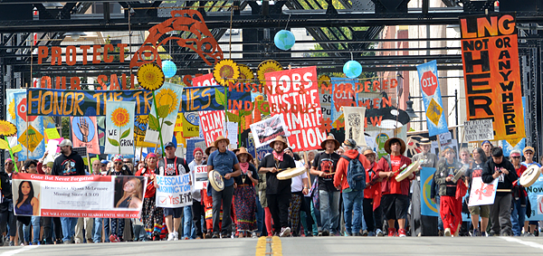 A group of indigenous protestors crossing a bridge holding colorful signs in protest of Fracked Gas and Fossil Fuels