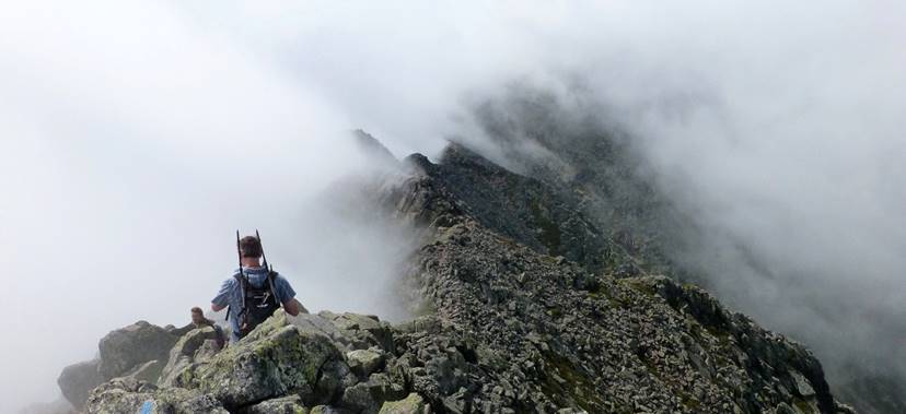 A couple hikers on The Knife Edge, Katahdin. Baxter Peak, 5267', the highest summit of Katahdin and the northern terminus of the Appalachian Trail, is 1/4 mi further along the ridge. Chimney Pond and the campground there are 2400' below to the right. This route is the trickiest on Katahdin, but is fine with strongish legs, reasonable preparation, and paying attention; there is good footing except when icy.