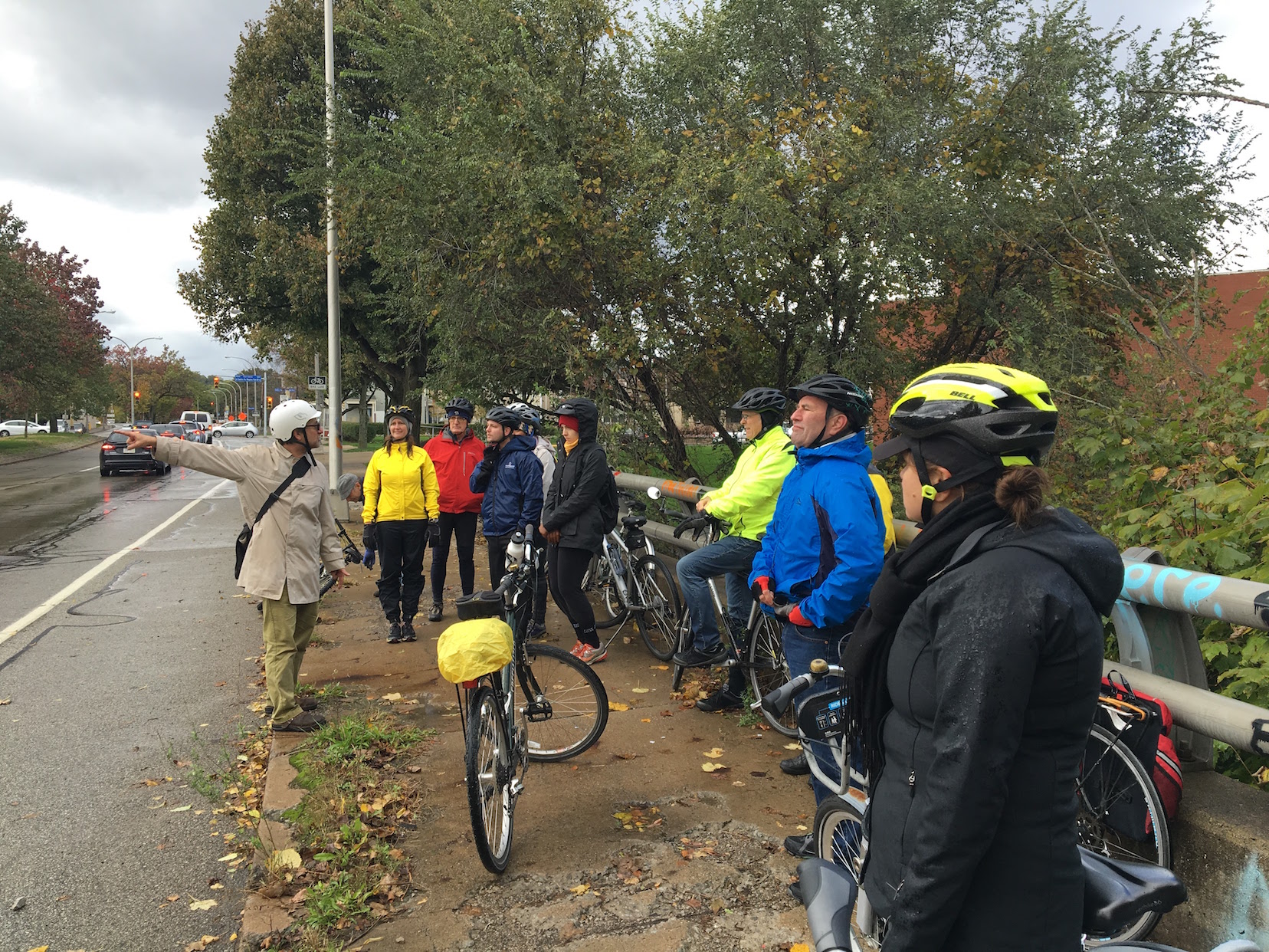 Photo of a man in a coat and helmet pointing out sewer infrastructure to a group of cyclists on a Sierra Club outing in Pittsburgh