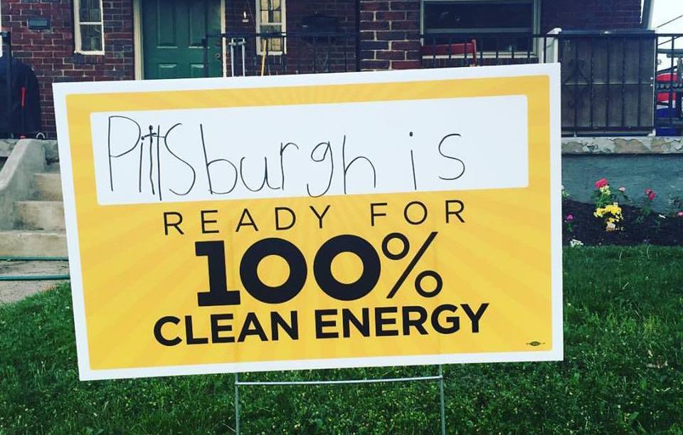 yard sign in front of red brick carpenter style house with handwritten "Pittsburgh is Ready for 100" in black and gold