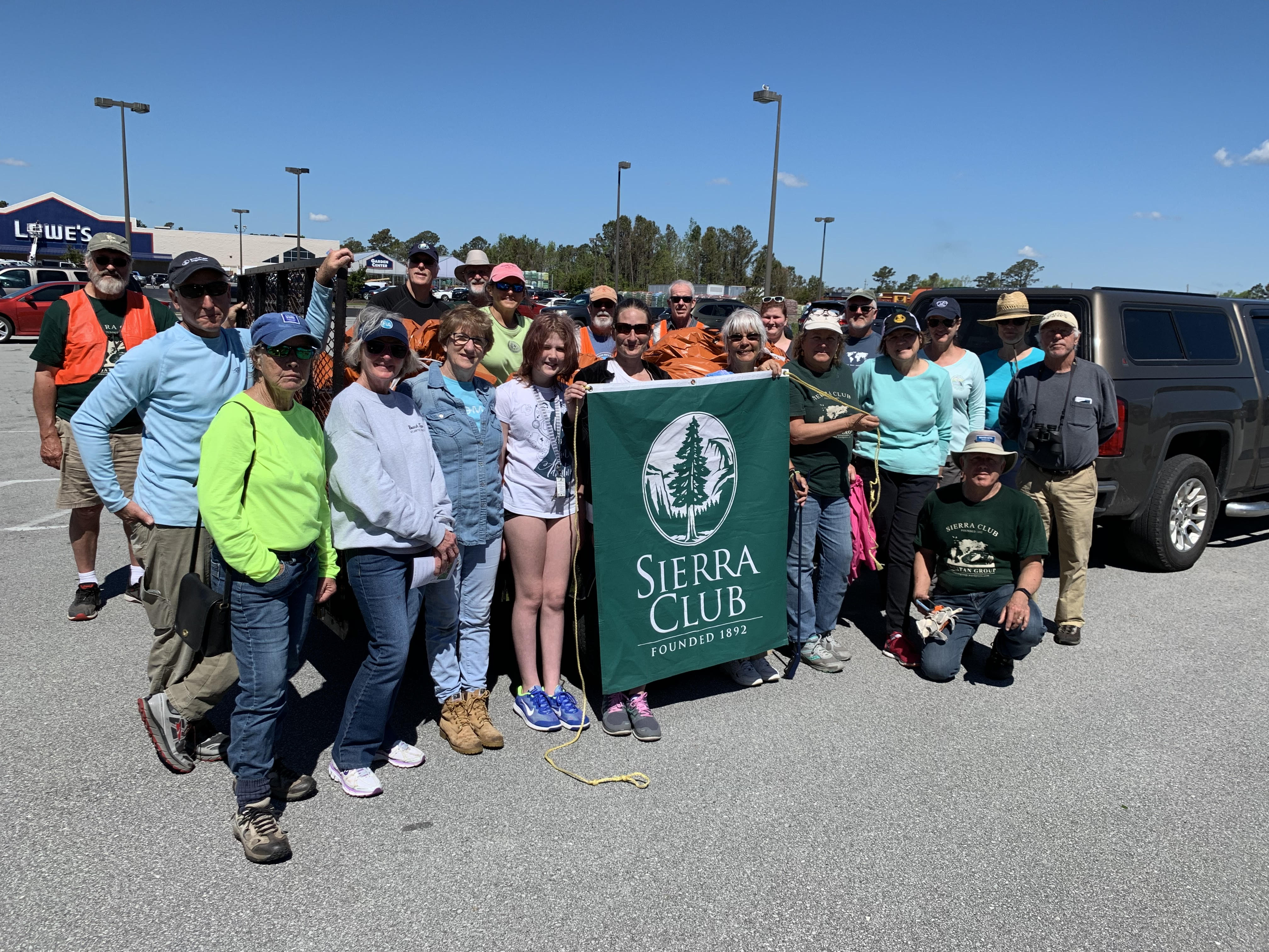 A group of approximately 20 people stand in a parking lot holding a Sierra Club banner