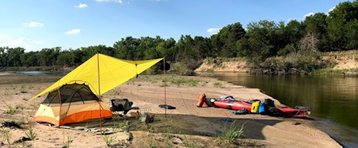 tent and kayak on sandy beach next to river