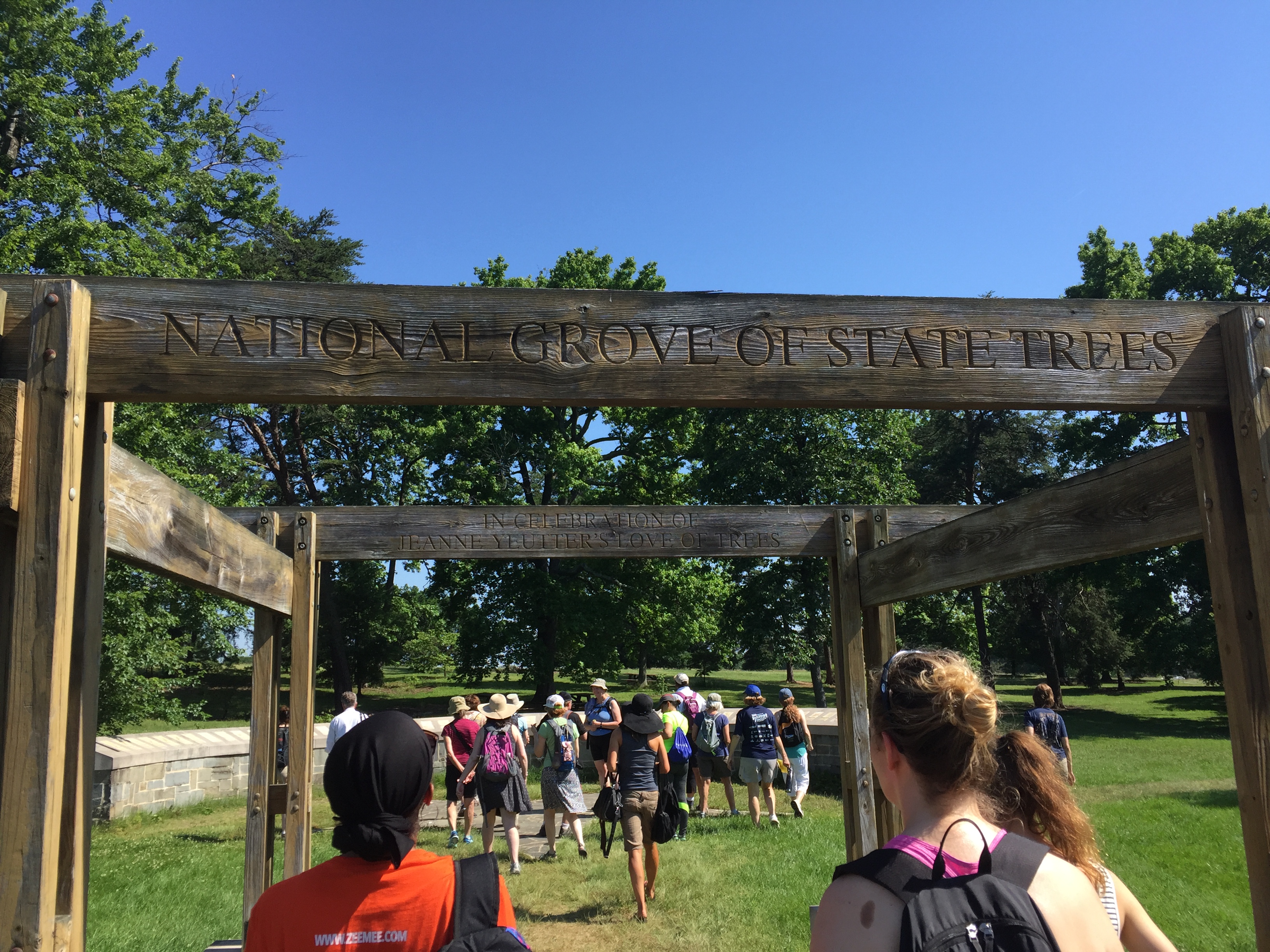 Hikers walk under an arch inscribed "National Grove of State Trees"